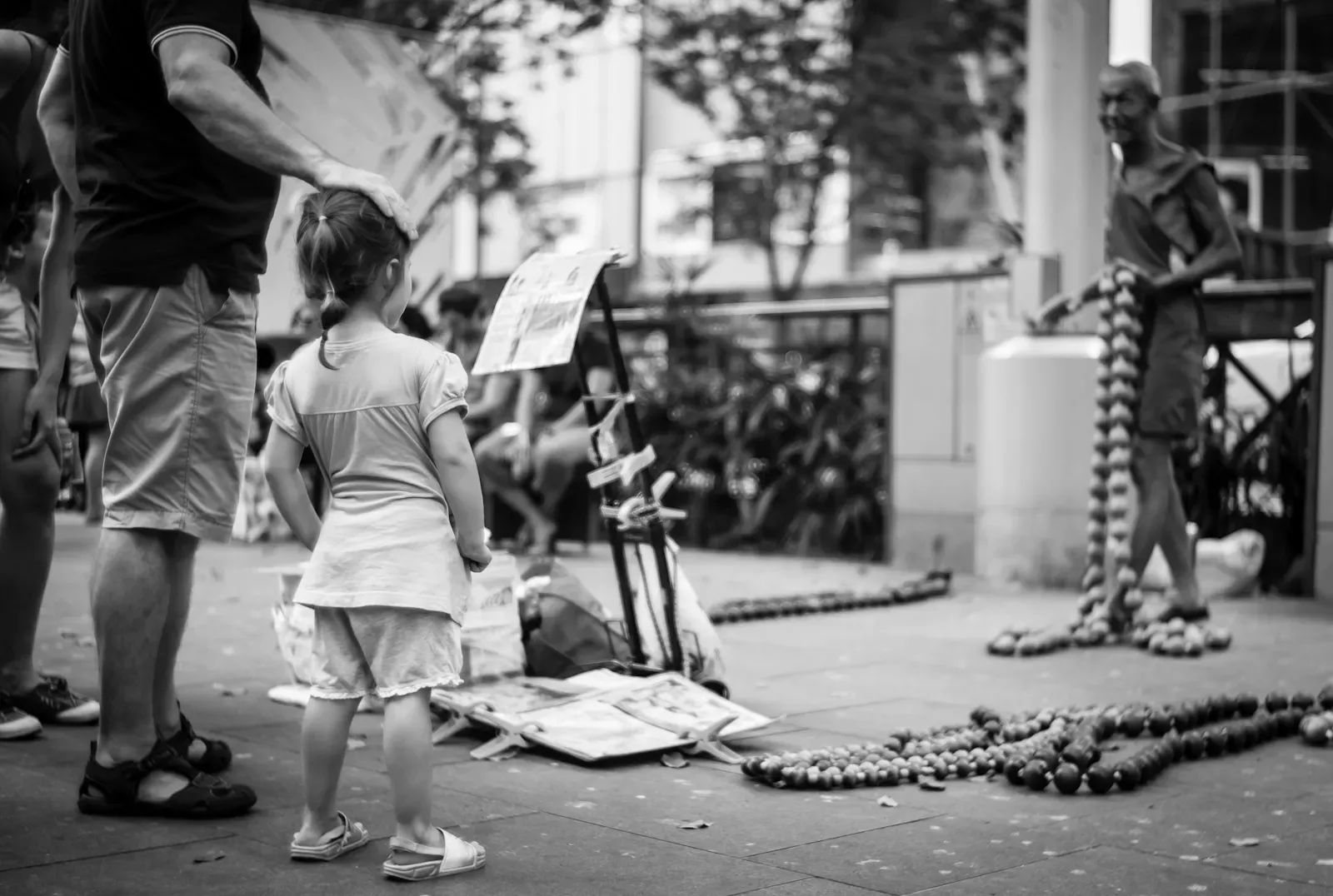 Man patting his daughter's head as she watches the street performer