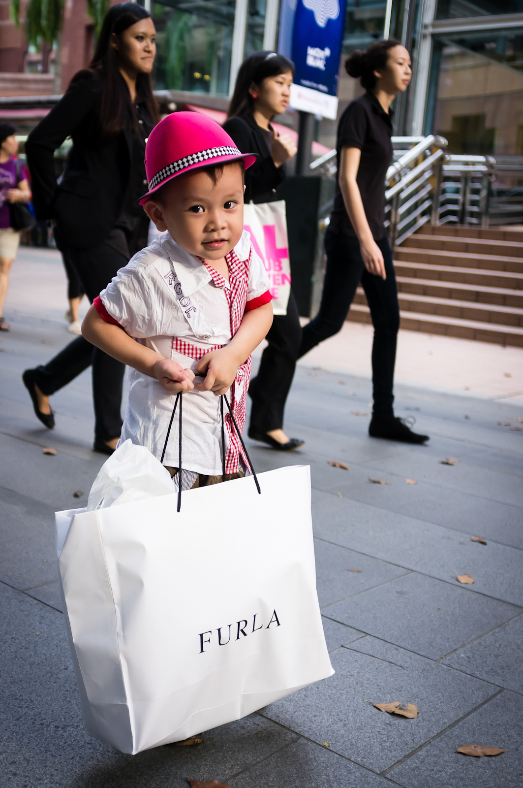 Street photography - Little boy with a pink hat helping to carry shopping bags